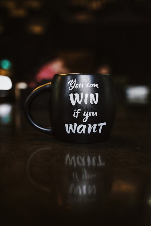 Free Black mug with inspirational quote 'You can win if you want' reflected on a dark surface, creating a motivational ambiance. Stock Photo